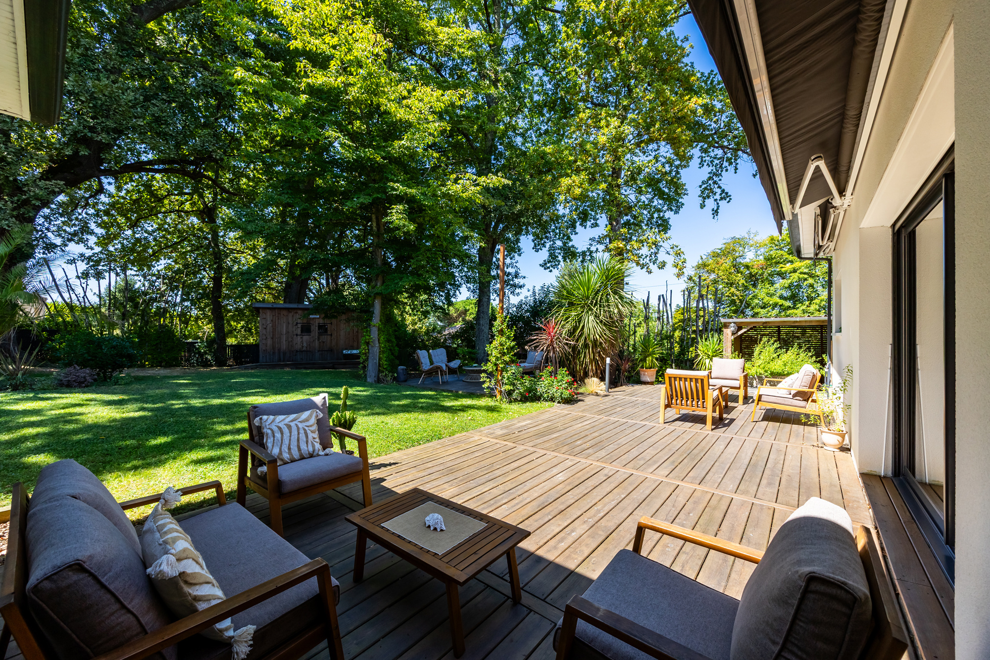 Terrasse de maison à Eysines Terrasse en bois avec mobilier de jardin dans un jardin verdoyant.