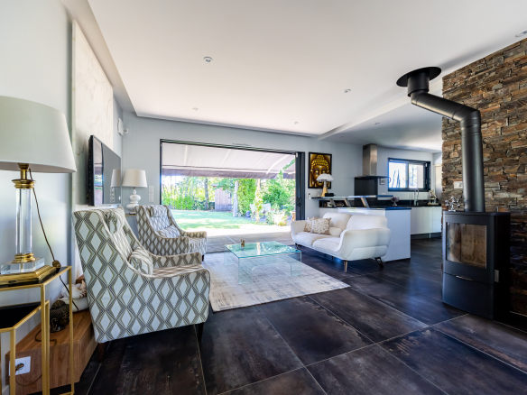 Intérieur d'une maison de plain pied moderne avec salon lumineux et cheminée, jardin visible à travers les baies vitrées.