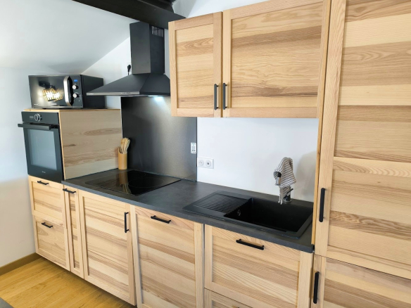 Cuisine moderne en bois clair avec plan de travail en noir, équipée d'un four et d'un évier.