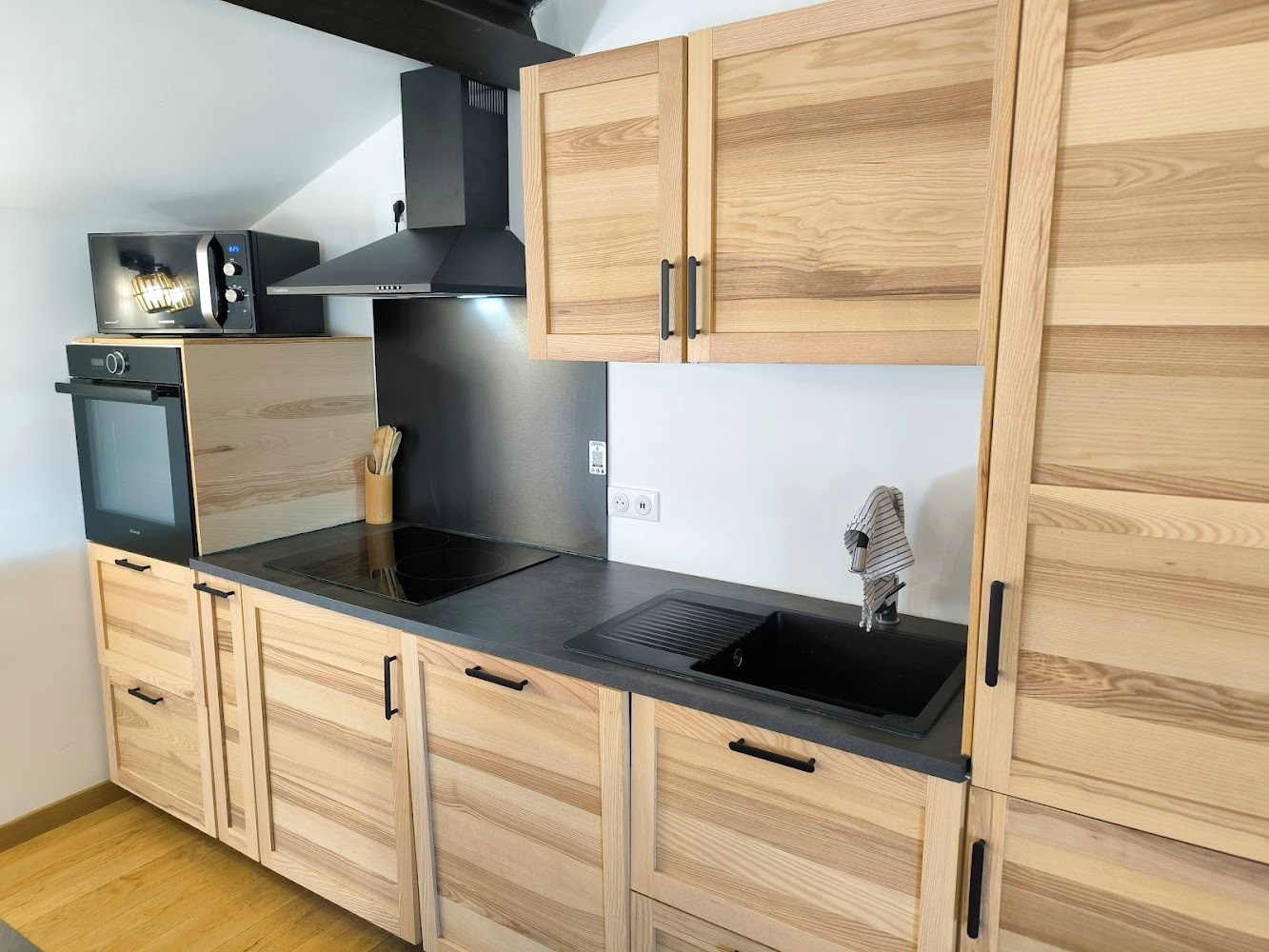 Cuisine d’un duplex à Bonnieux Cuisine moderne en bois clair avec plan de travail en noir, équipée d'un four et d'un évier.