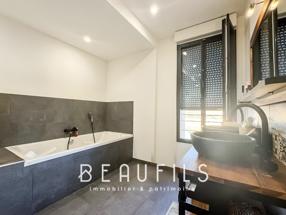 Salle de bain moderne avec baignoire et lavabo, murs en carrelage gris et noir.