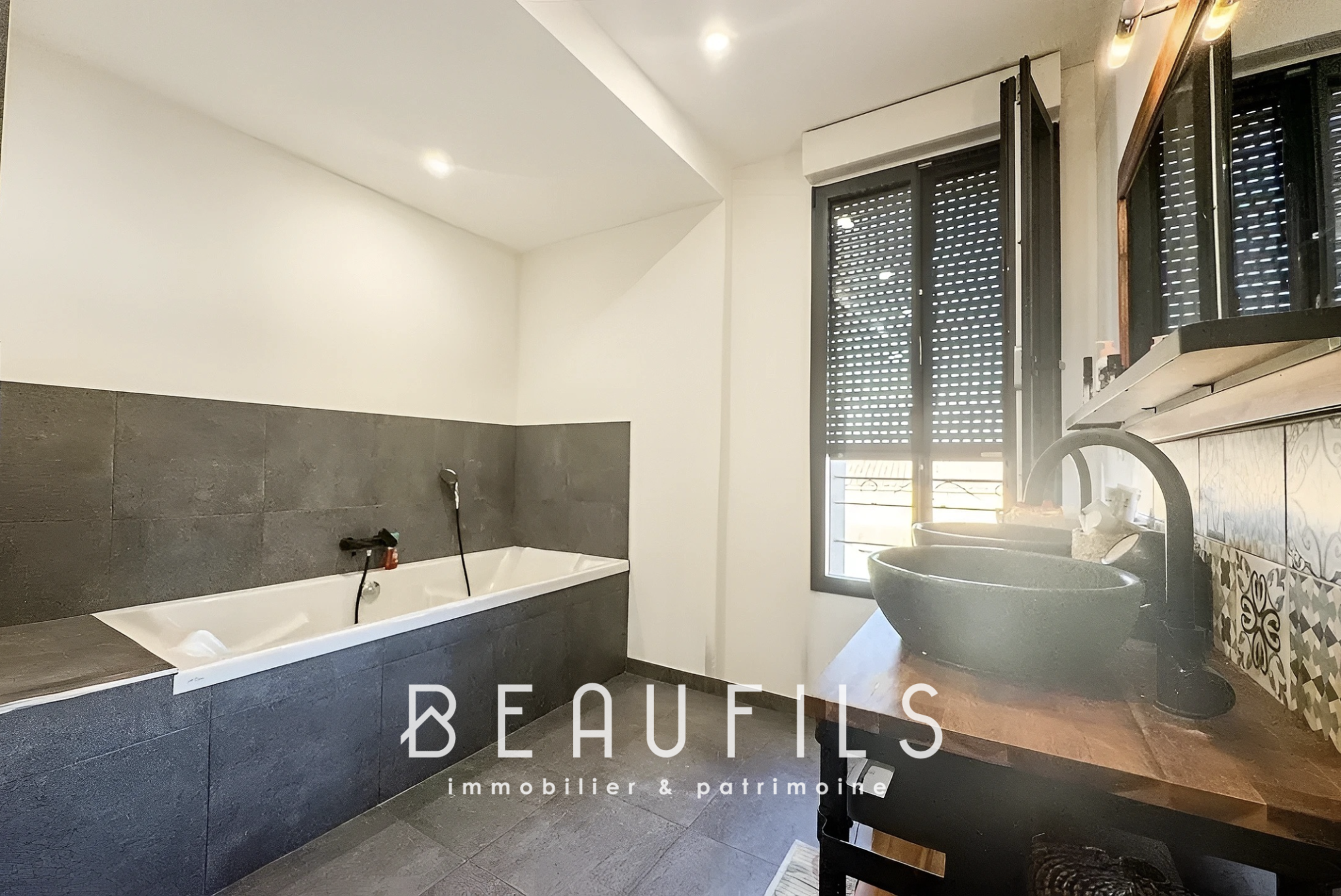 Salle de bain du loft à Mauguio Salle de bain moderne avec baignoire et lavabo, murs en carrelage gris et noir.