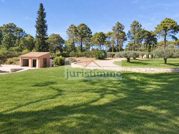 Vue d'un jardin paysager avec pelouse verte et arbres, incluant un bâtiment en pierre.