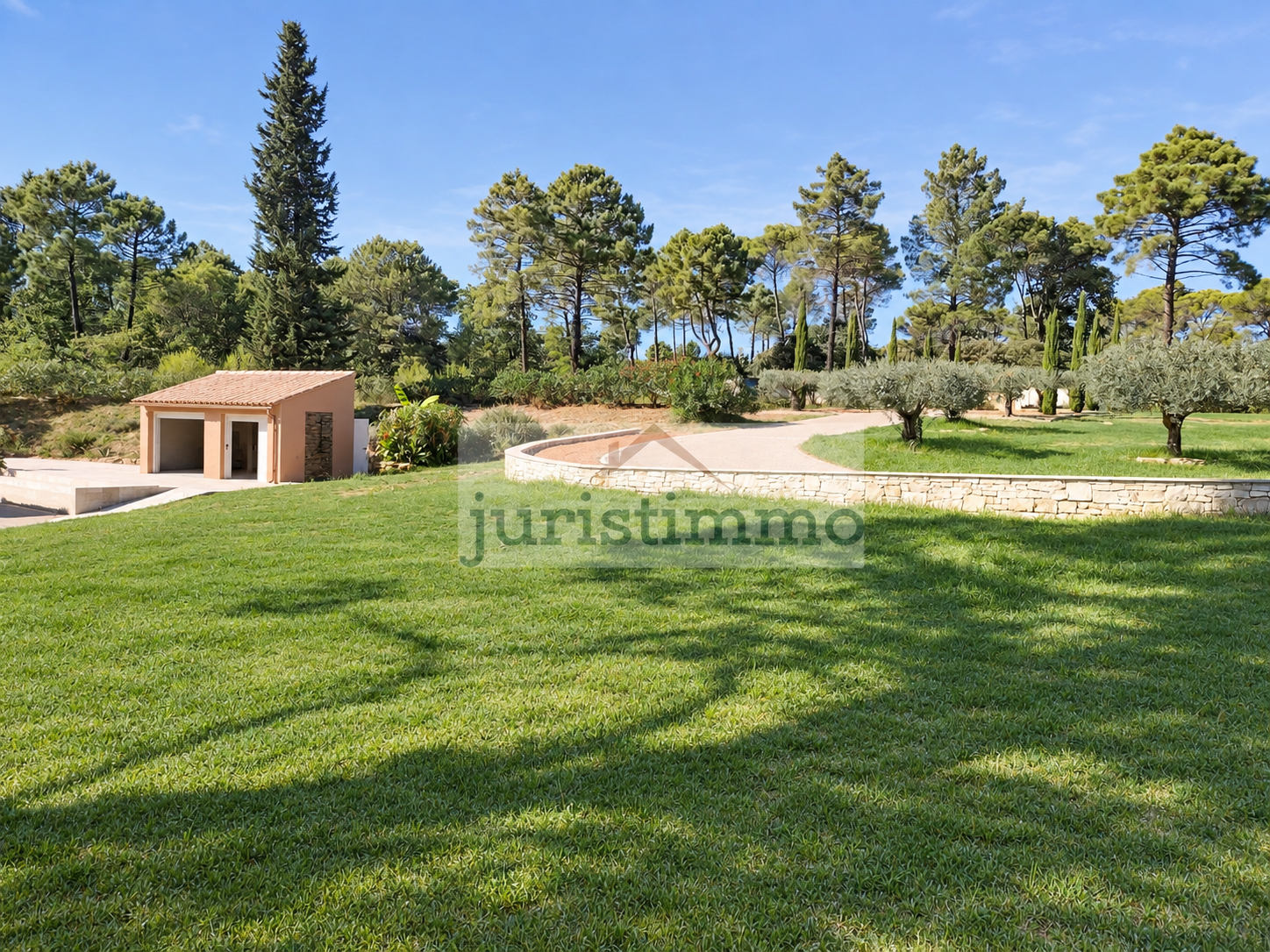 Propriété architecte avec jardin à Uchaux Vue d'un jardin paysager avec pelouse verte et arbres, incluant un bâtiment en pierre.