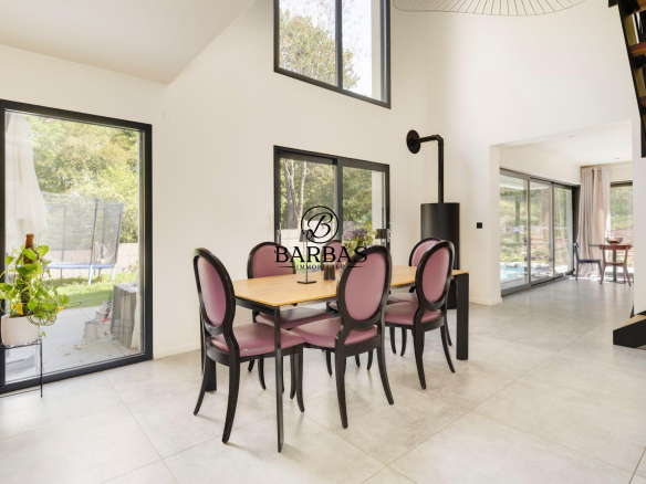 Intérieur d'une maison contemporaine avec salle à manger et grandes fenêtres donnant sur l'extérieur.