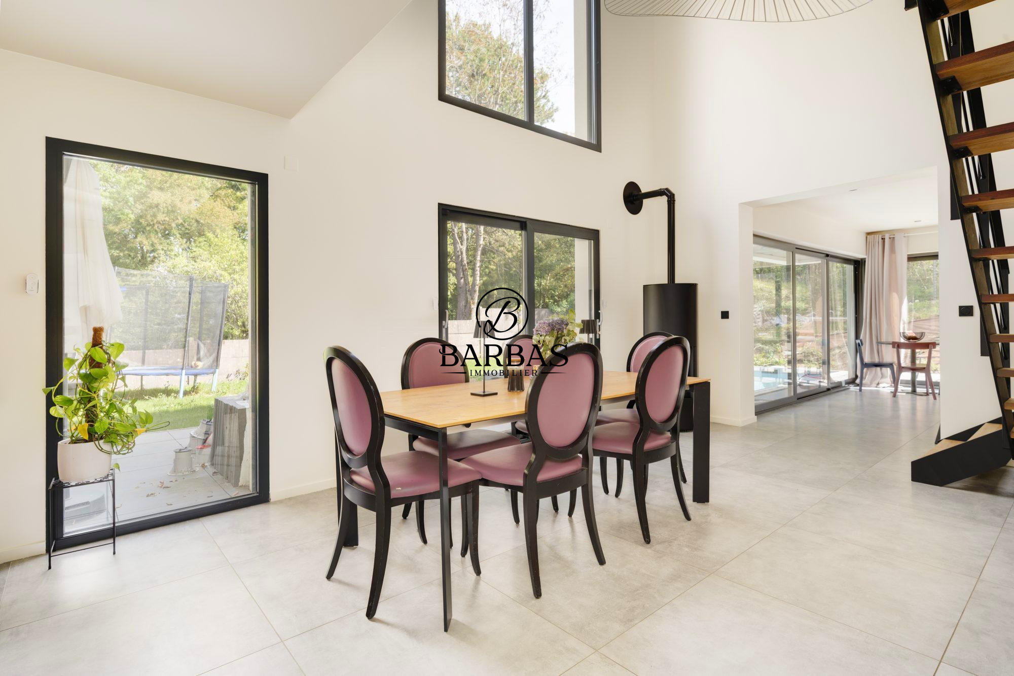Intérieur d'une maison contemporaine avec salle à manger et grandes fenêtres donnant sur l'extérieur.