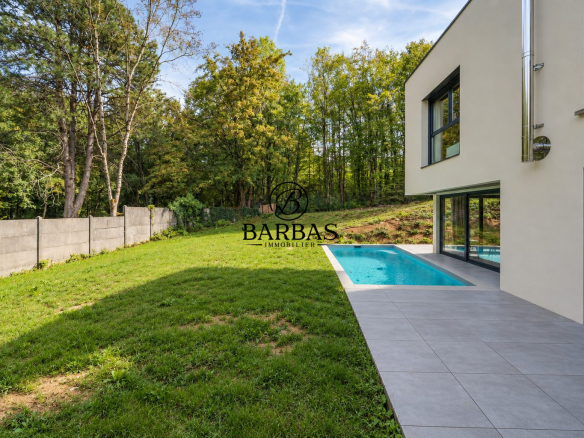 Maison d'architecte contemporaine avec piscine, jardin verdoyant et forêt à proximité.