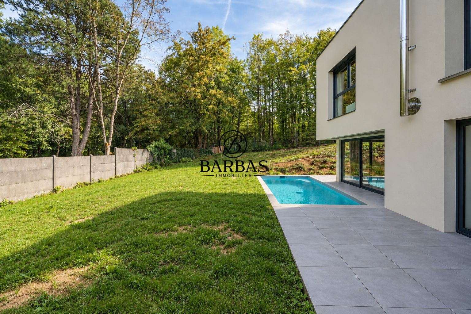 Maison d'architecte contemporaine avec piscine, jardin verdoyant et forêt à proximité.