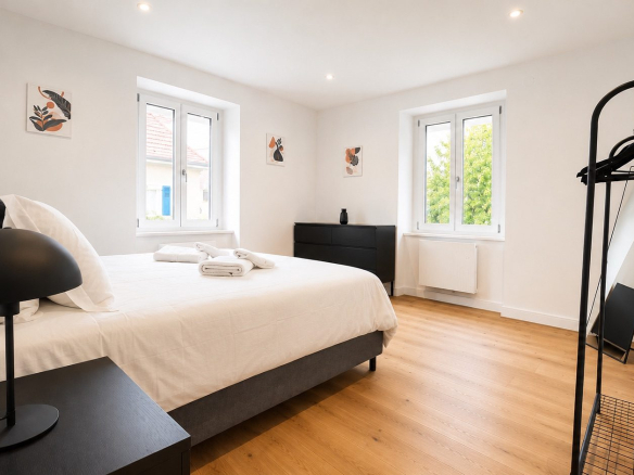 Chambre d'une maison rénovée avec lit double, mobilier moderne et lumière naturelle à Munster.