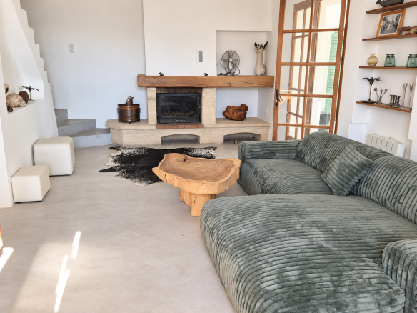 Intérieur d'une maison avec un salon spacieux et une cheminée, éclairé par la lumière naturelle.