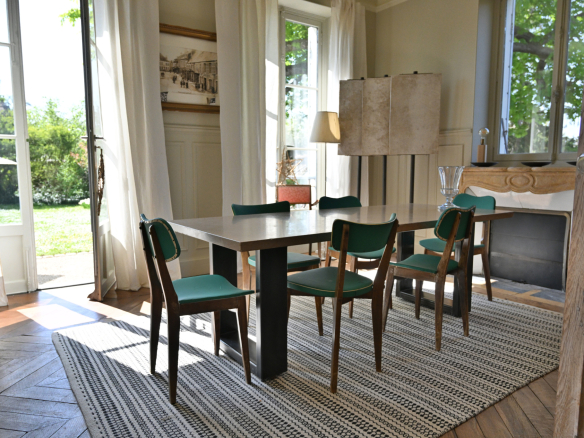 Salle à manger lumineuse avec table et chaises, fenêtres ouvertes sur jardin.