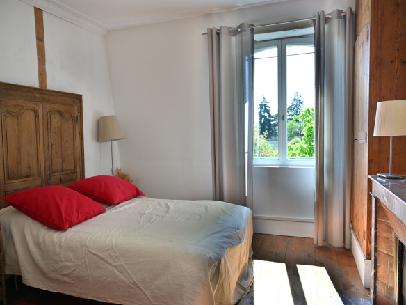 Chambre d'une maison de caractère avec lit double et fenêtre offrant une vue sur l'extérieur.