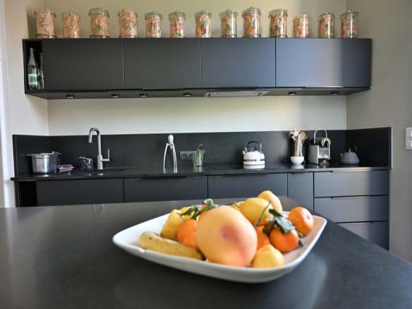 Cuisine moderne avec plan de travail noir et fruits sur une assiette, étagères au-dessus avec bocaux en verre.