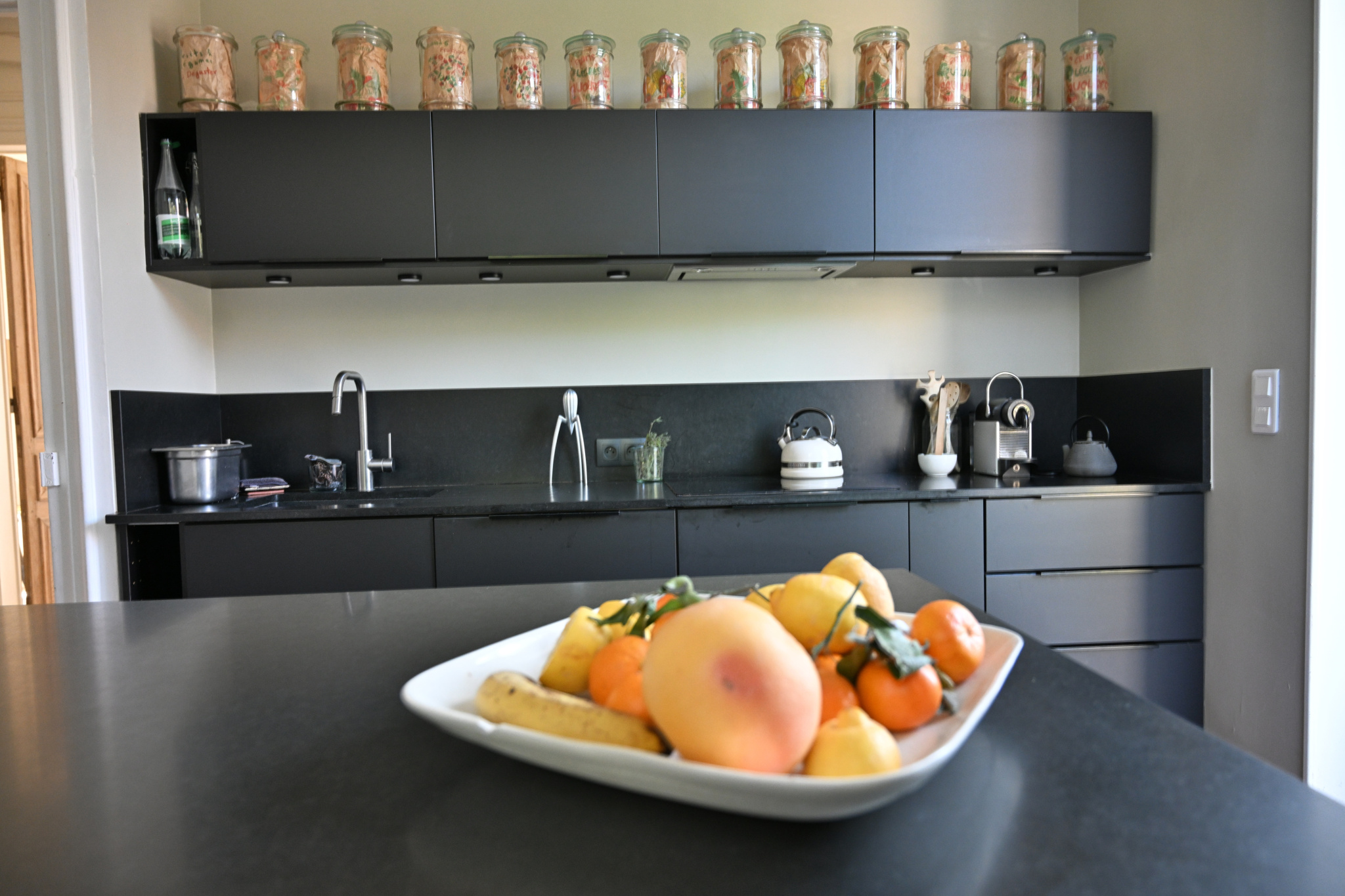 Cuisine moderne et élégante Cuisine moderne avec plan de travail noir et fruits sur une assiette, étagères au-dessus avec bocaux en verre.