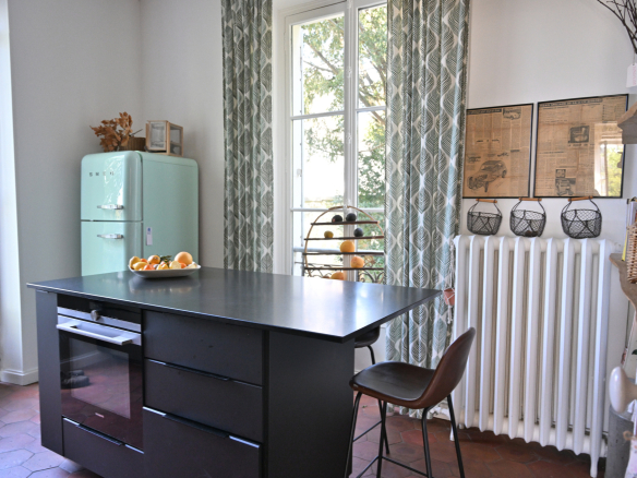 Cuisine d'une maison de caractère avec un îlot central et un réfrigérateur vintage, fenêtres ouvertes sur l'extérieur.
