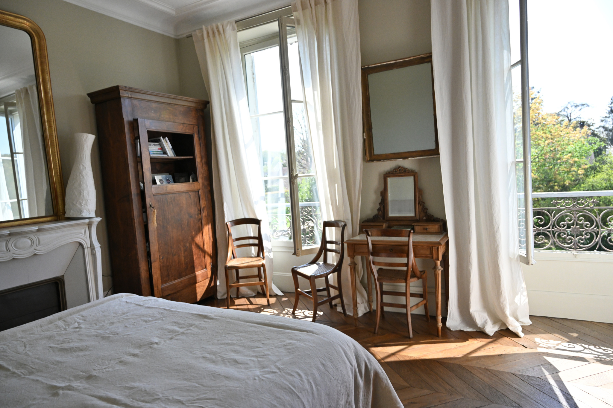 Chambre élégante dans une maison de caractère Intérieur d'une chambre avec un lit, des chaises en bois et une commode, fenêtres ouvertes sur un jardin.