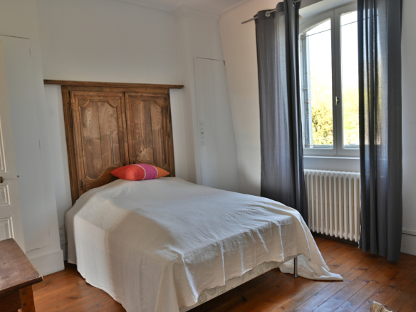 Chambre d'une maison de caractère avec lit simple et fenêtre laissant entrer la lumière.