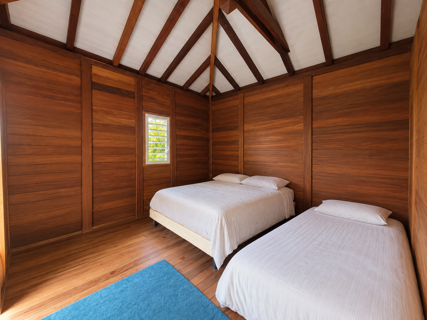 Chambre d'une maison en bois avec deux lits et murs en bois à Goyave.