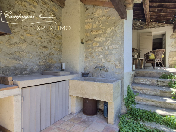 Outdoor stone kitchen with barbecue and living area, in a restored farmhouse in Maubec.