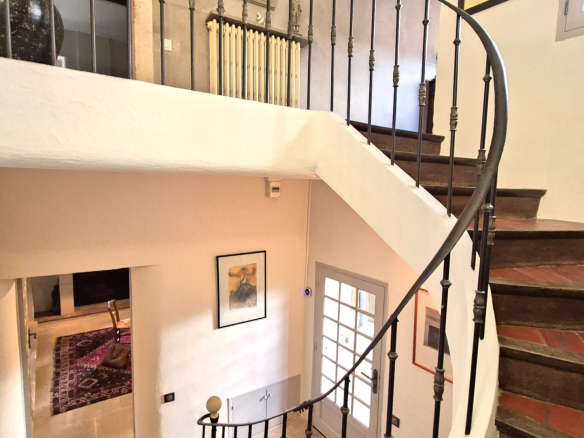 Spiral staircase in a restored farmhouse with light walls and works of art.
