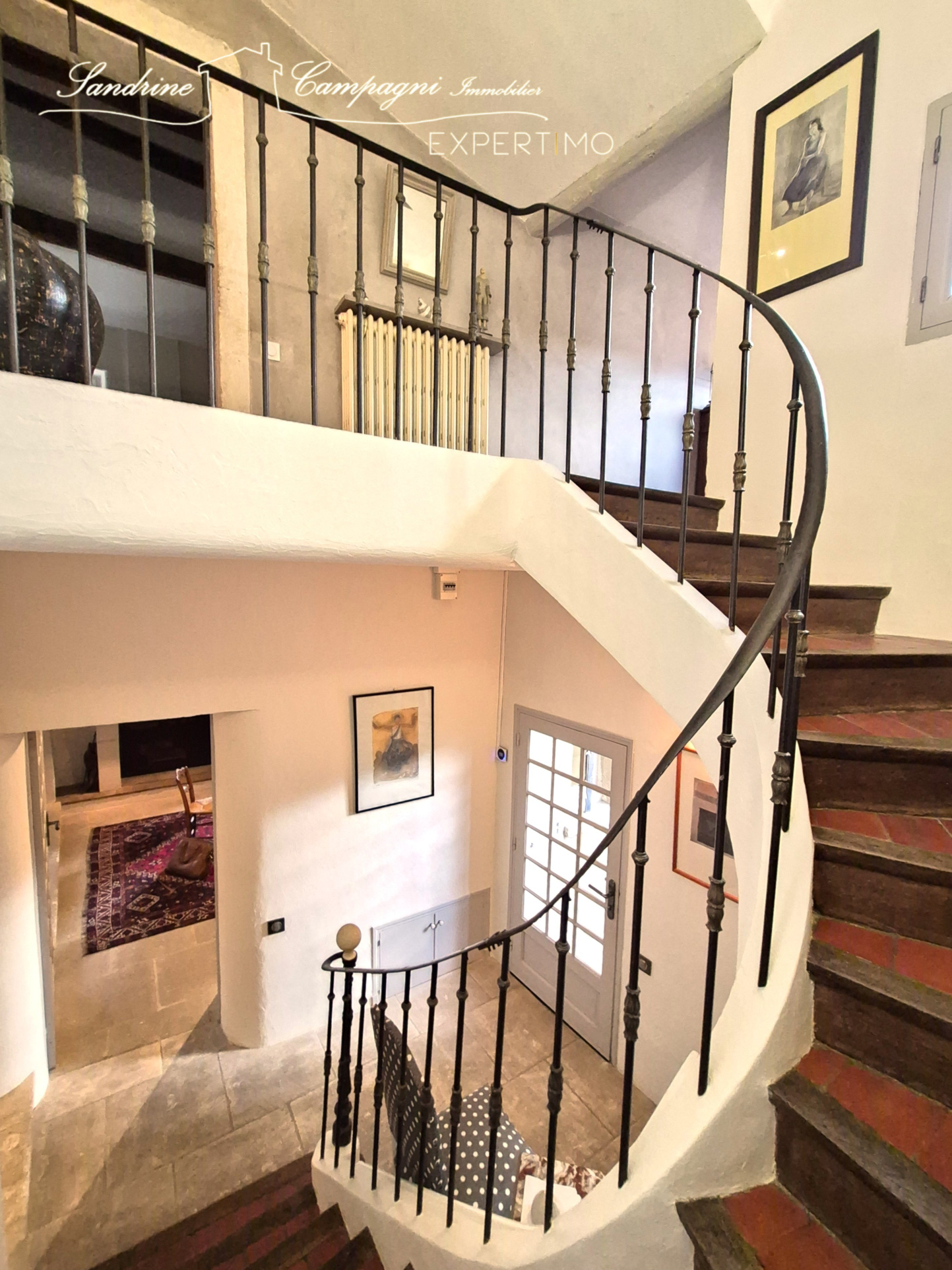Restored staircase of the farmhouse in Maubec Spiral staircase in a restored farmhouse with light walls and works of art.
