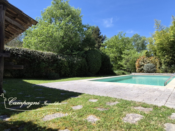 Swimming pool and landscaped area around an old farmhouse in Maubec, with lawn and trees.