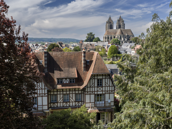 Elegant townhouse in Noyon with a view of the cathedral, surrounded by trees.
