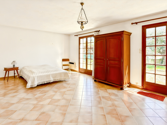 Interior of a spacious bedroom with a bed, a wooden piece of furniture and windows overlooking the outside.