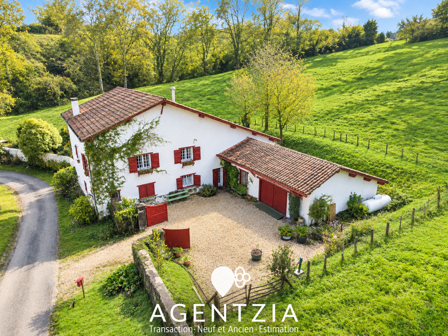 17th century Labourdine farmhouse in Cambo-les-Bains, surrounded by greenery and a tree-lined path.