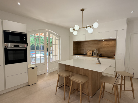 Modern kitchen with central island and designer lighting, open to the outside.