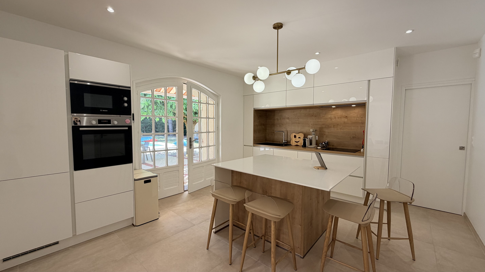 Modern kitchen with central island and designer lighting, open to the outside.