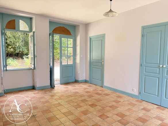 Interior of a longère with light walls and blue doors, offering a view of a wooded area.