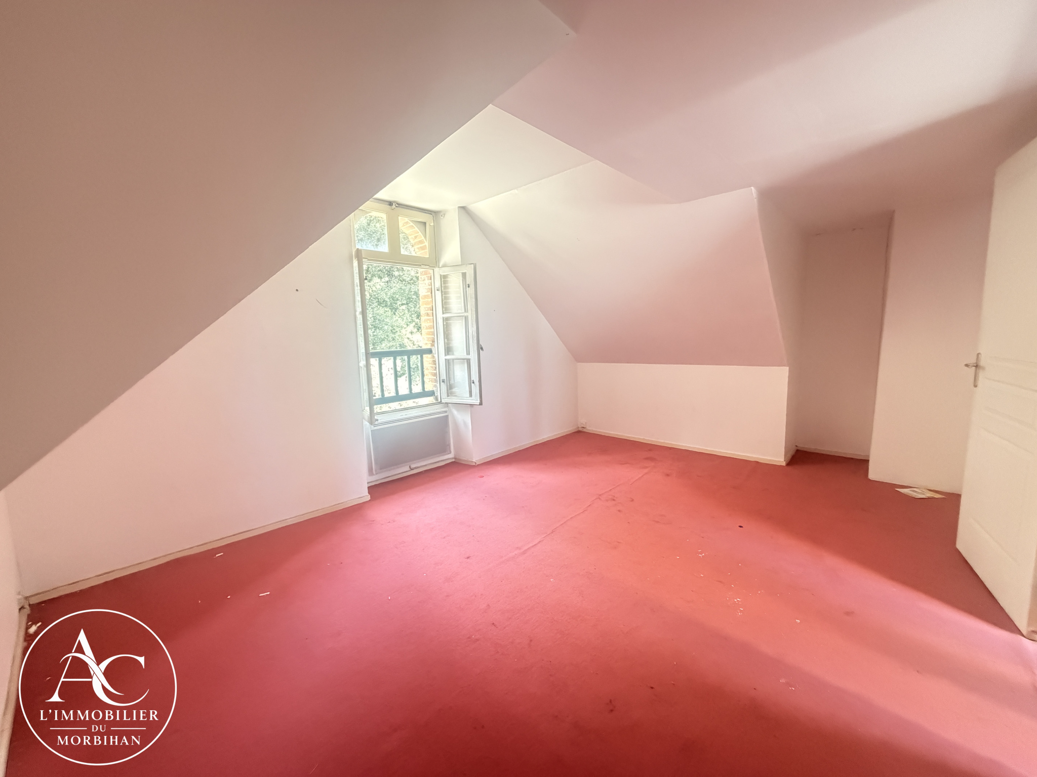 Room in a farmhouse in Sarzeau Interior of a bedroom with red carpet and a window overlooking a wooded area.