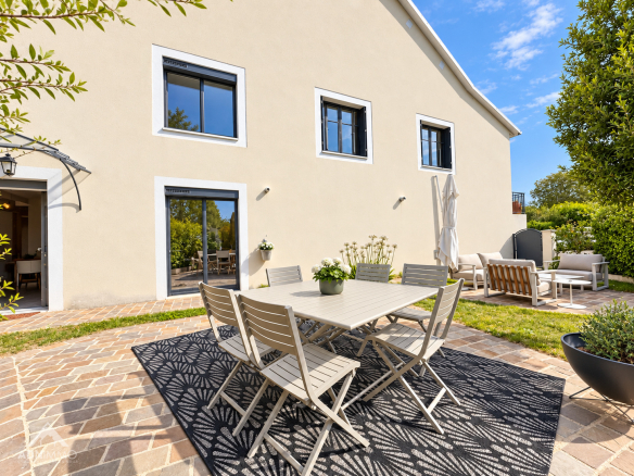 Terrasse d'une maison rénovée avec table et chaises, entourée de verdure à Saint-Genis-Pouilly.