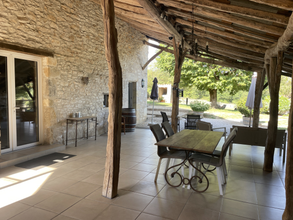 Covered terrace of a stone house with table and chairs, overlooking the garden