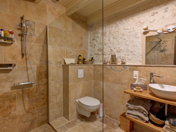 Modern bathroom with shower and sink, stone walls and beige tiles.