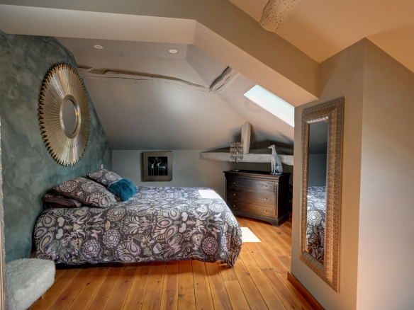 Elegant room with double bed, modern decor and mirror, under a sloping ceiling.