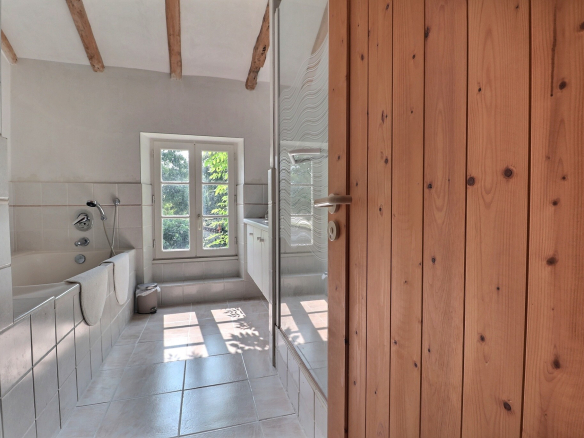 Salle de bain lumineuse avec baignoire et fenêtre, murs carrelés et plafond à poutres apparentes.