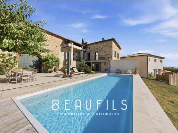Domaine avec piscine et mas historique en pierre, entouré de verdure et collines.
