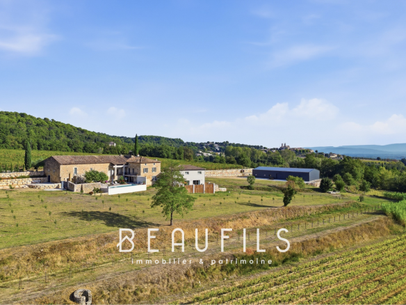 Vue panoramique d'un domaine avec vignoble et mas historique en pierre, entouré de collines.