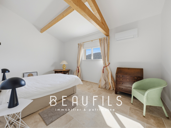 Chambre lumineuse avec plafond à poutres apparentes et mobilier moderne.