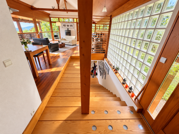 Intérieur d'une maison d'architecte avec un escalier en bois et des murs en verre.