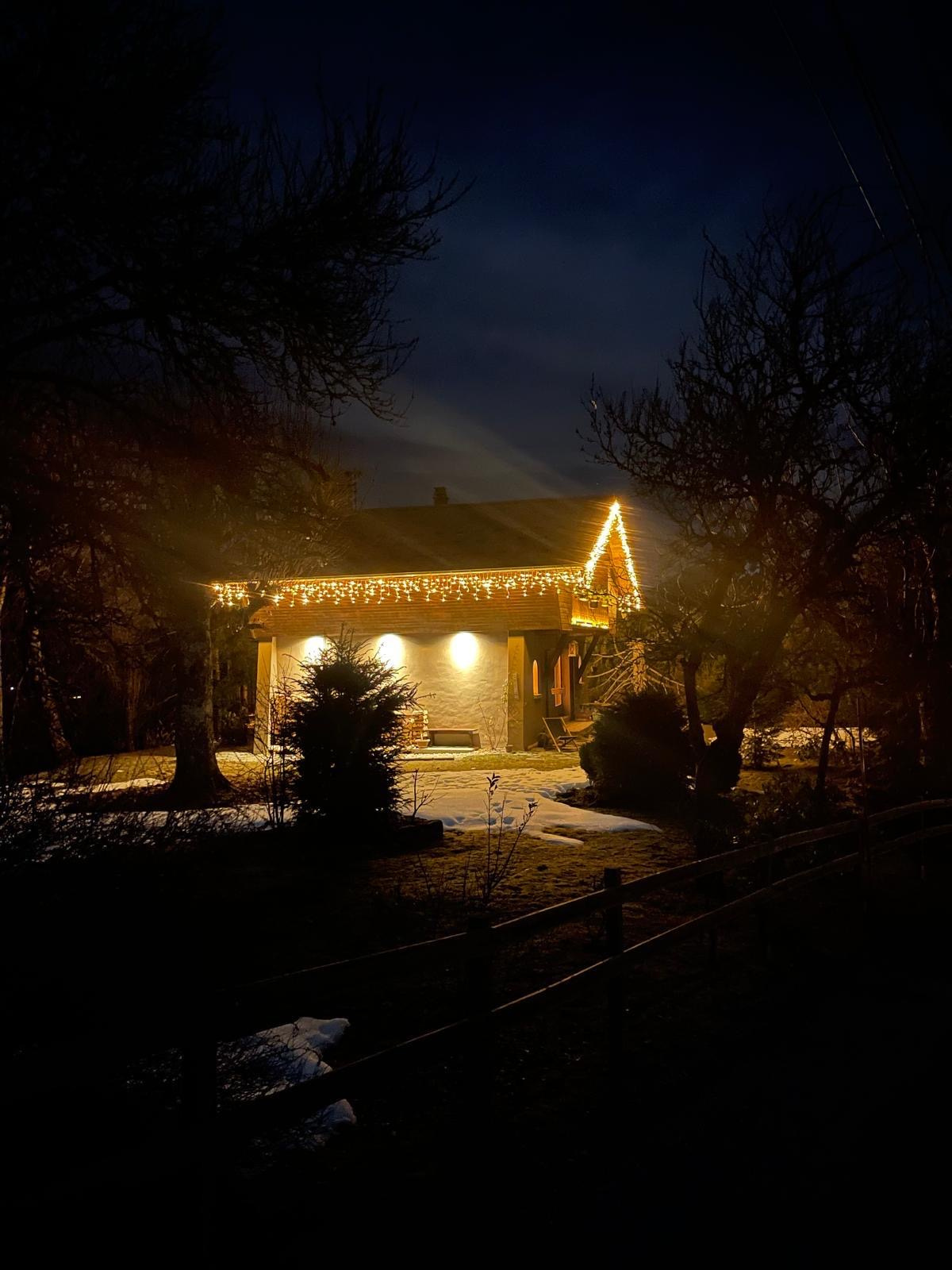 Chalet illuminé la nuit avec des décorations lumineuses, entouré d'arbres et de neige.