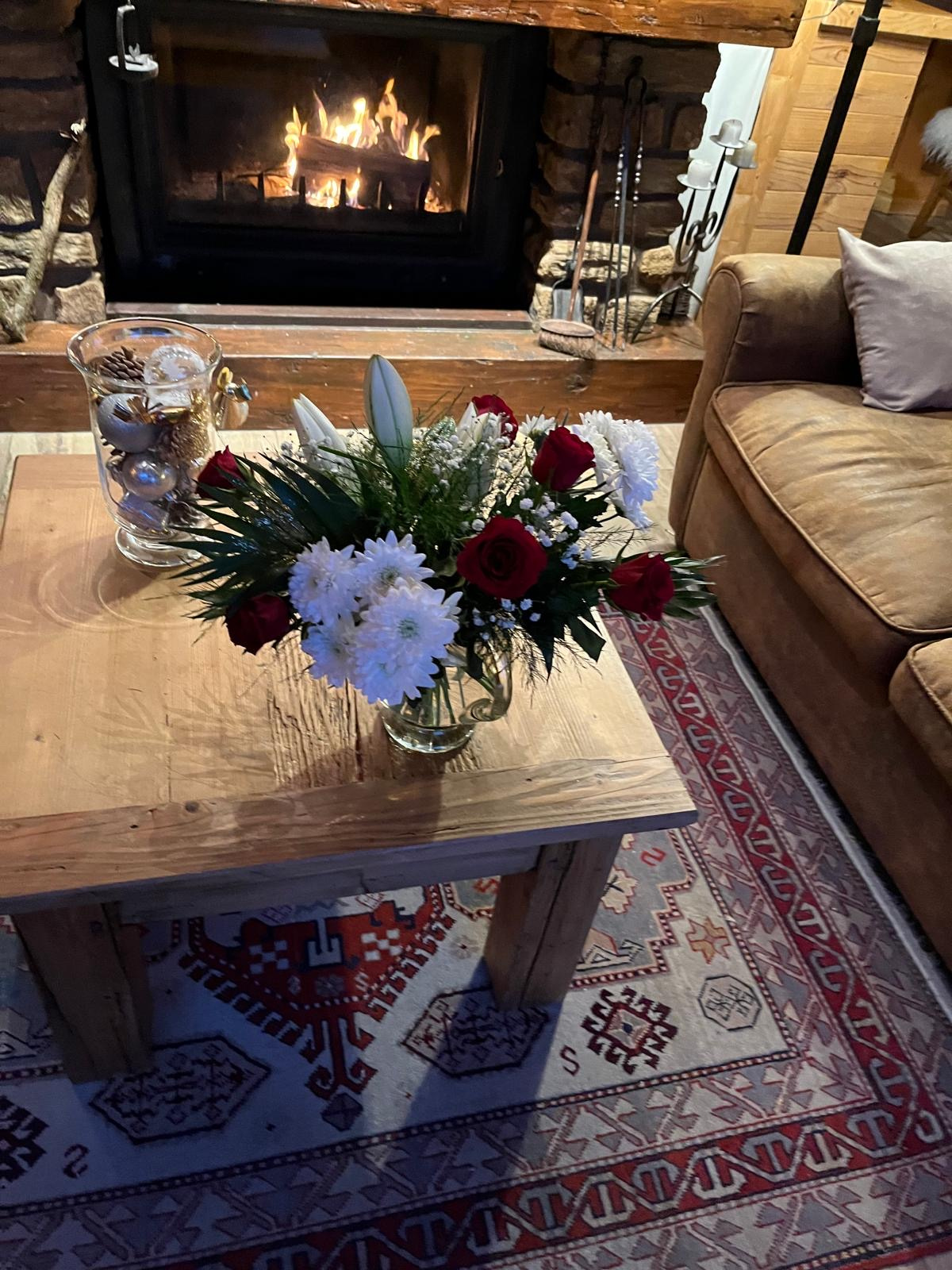 Intérieur d'un chalet avec un bouquet de fleurs sur une table en bois et un feu de cheminée.