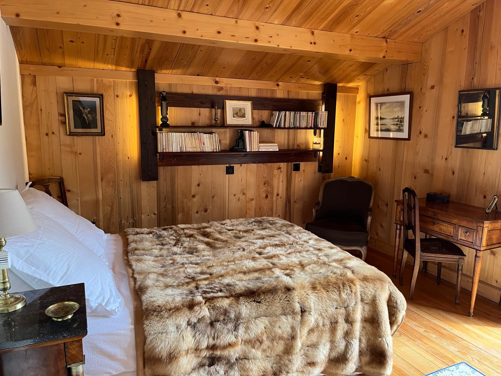 Chambre d'un chalet en bois avec lit, bureau et étagères, décorée de manière chaleureuse.