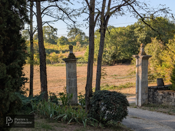 Entrée d'une propriété avec des piliers en pierre et un chemin menant à un parc arboré.