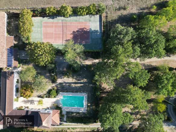 Vue aérienne d'une propriété avec piscine et terrain de tennis, entourée d'arbres.