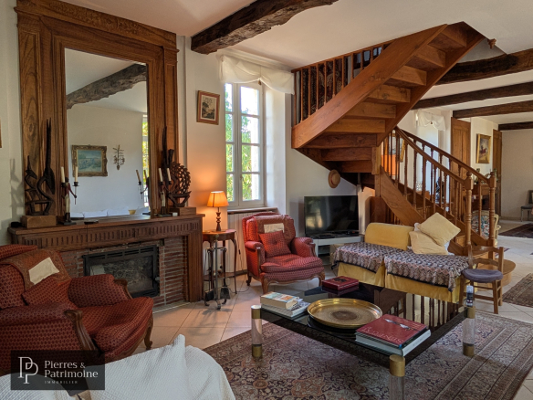 Intérieur d'une maison de caractère à Nérac, salon avec cheminée et escalier en bois.
