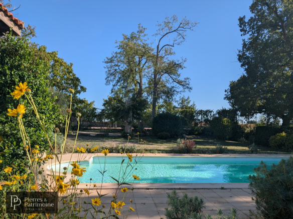 Vue sur une piscine entourée de fleurs et d'arbres dans un parc arboré.