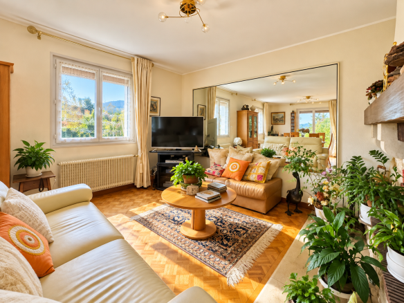 Intérieur d'une maison avec un salon lumineux, des plantes et un téléviseur.